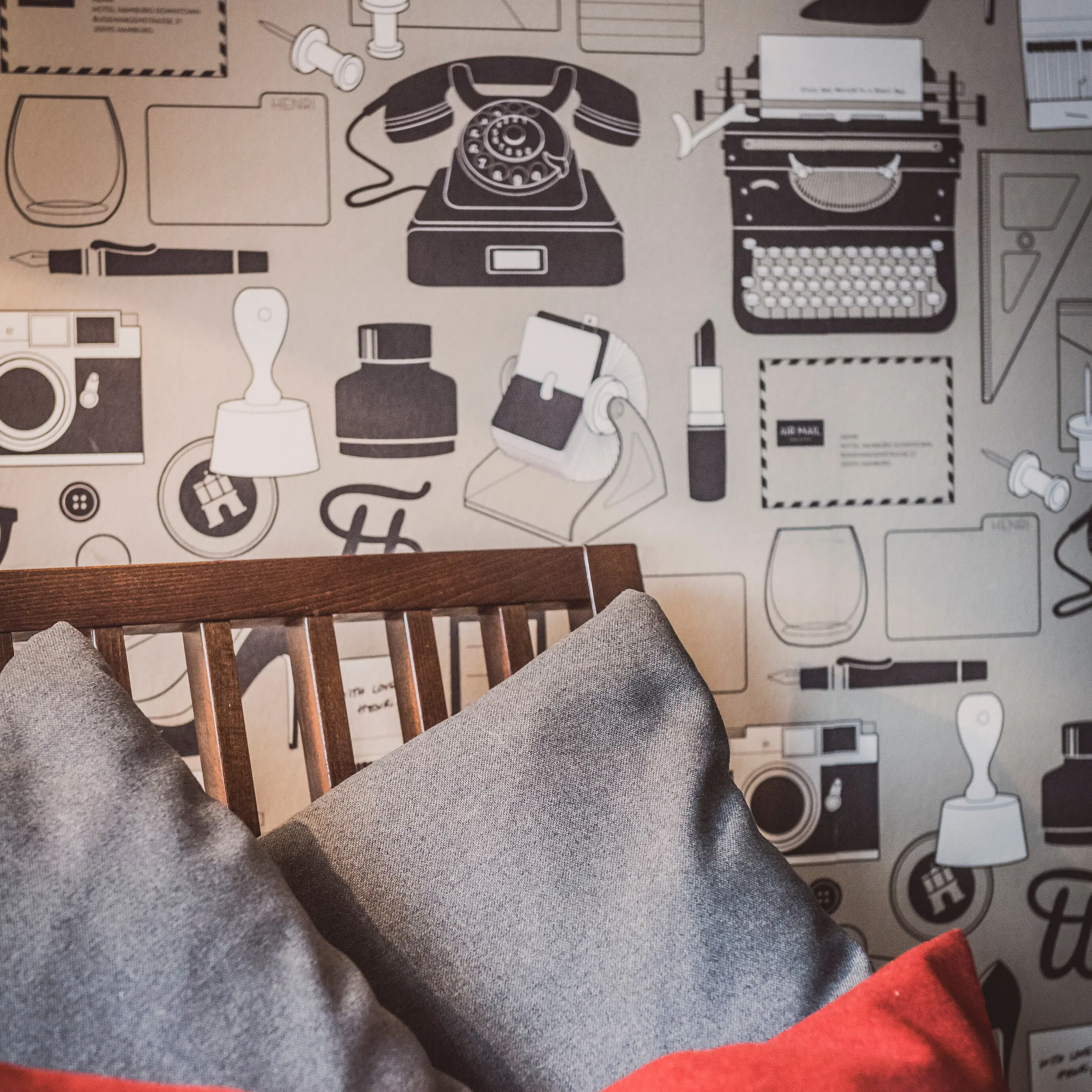 Armchair with grey and red cushions in front of a wall with motif wallpaper