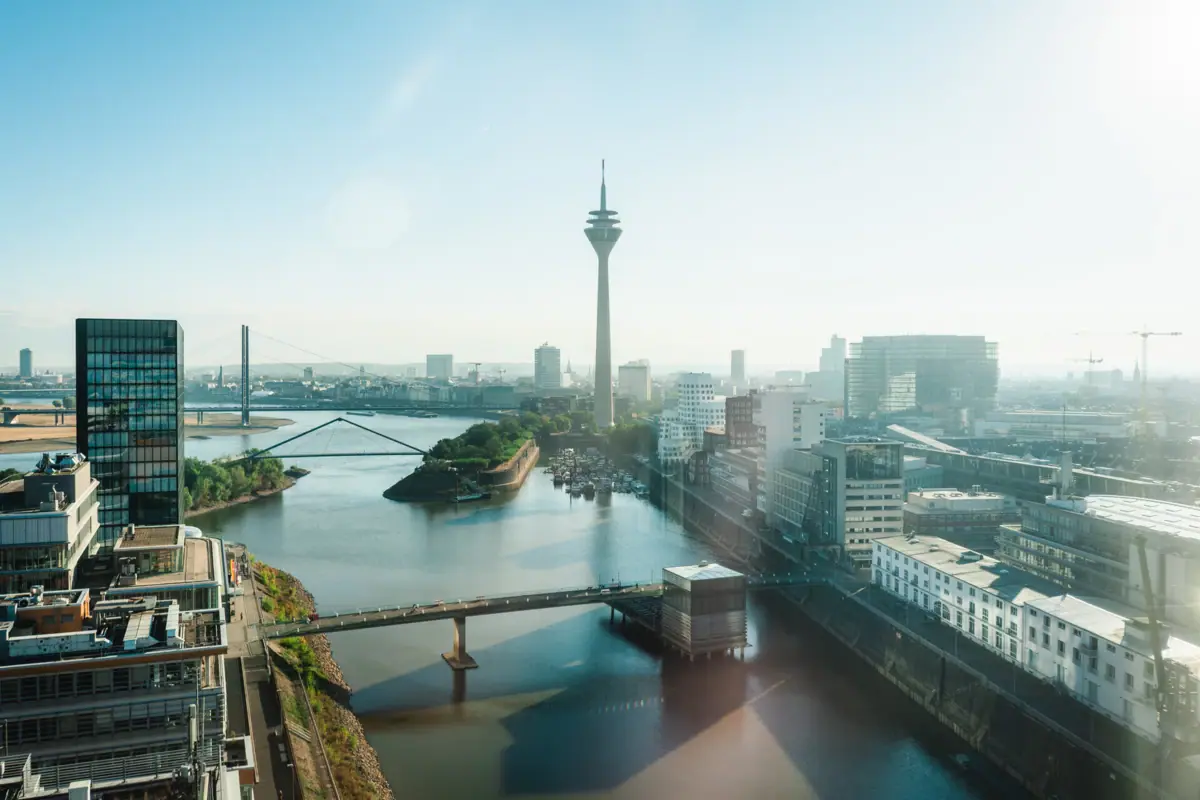 A cityscape featuring a river, a bridge and a tower.