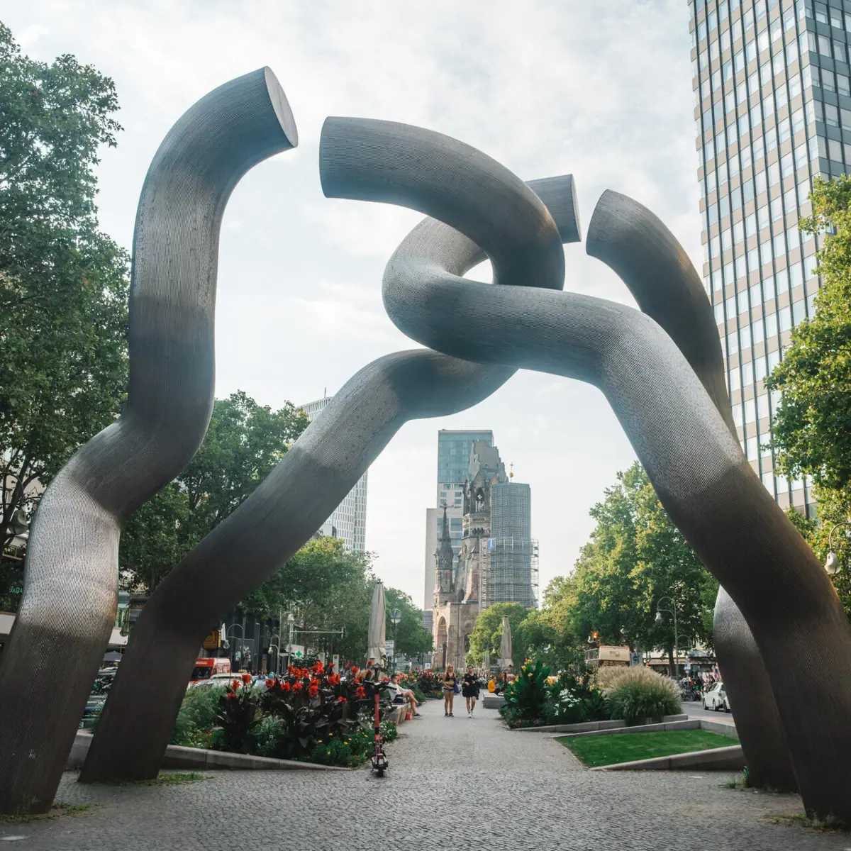 Sculpture of twisted metal pieces in an urban setting with a clear sky.