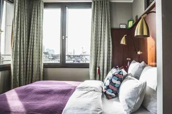 HENRI Düsseldorf A bed with pillows and a lamp in a room with windows.