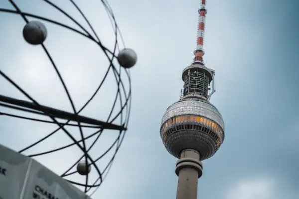 Berlin's Alexanderplatz with a high round tower in front of a blue sky with clouds.