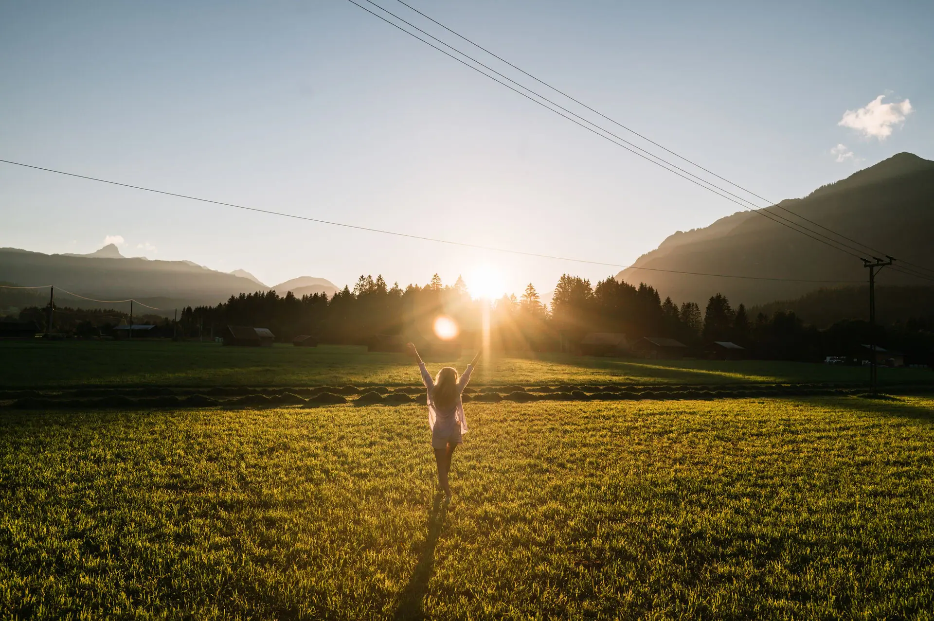 A woman is standing in a field with her arms raised.