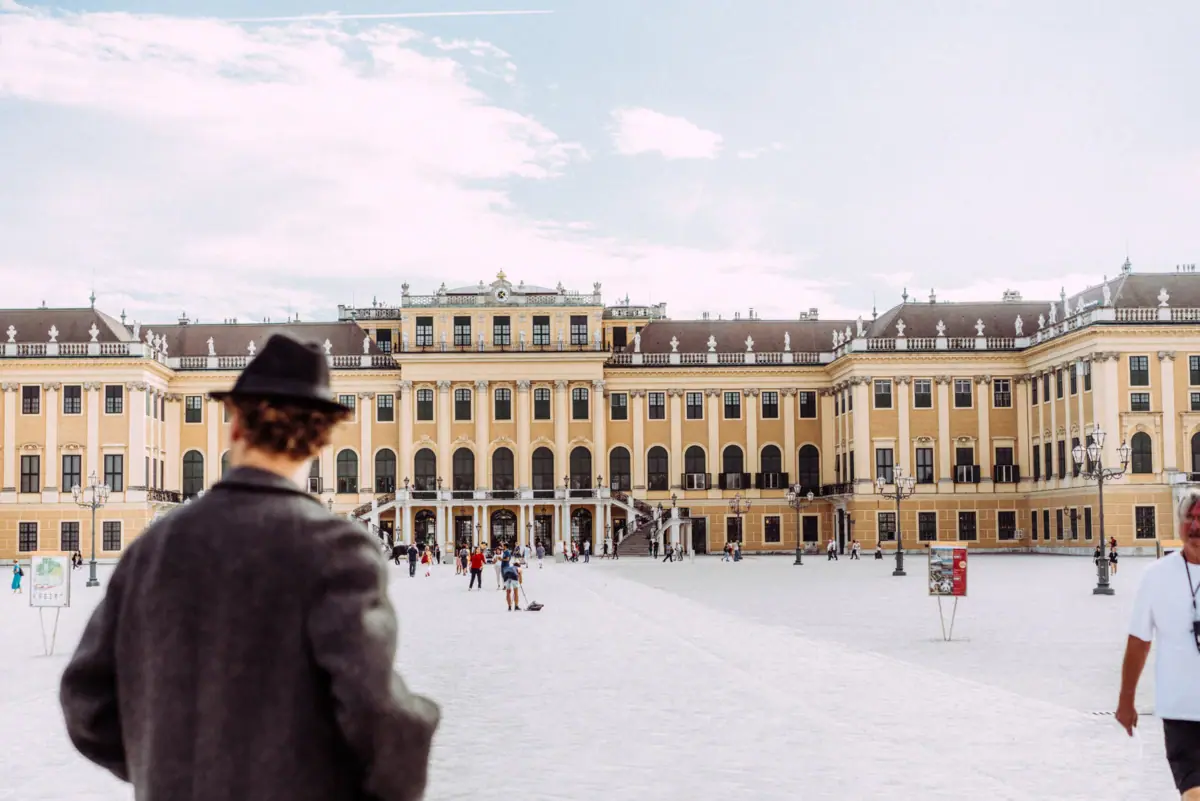 A man in a hat looks at a large building against the backdrop of Schönbrunn Palace.