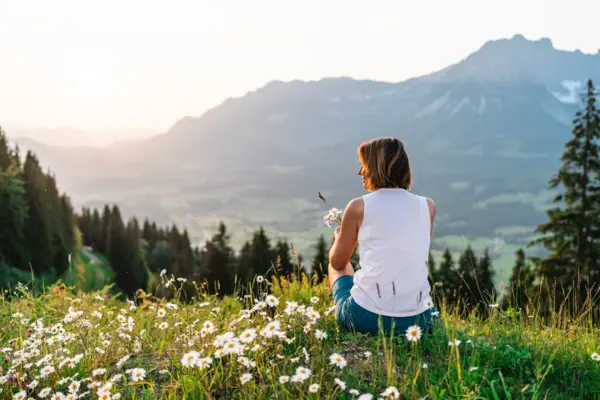 A woman sits on a hill with flowers.