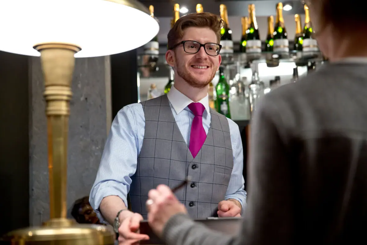 A man in a waistcoat and tie is standing at a reception desk.