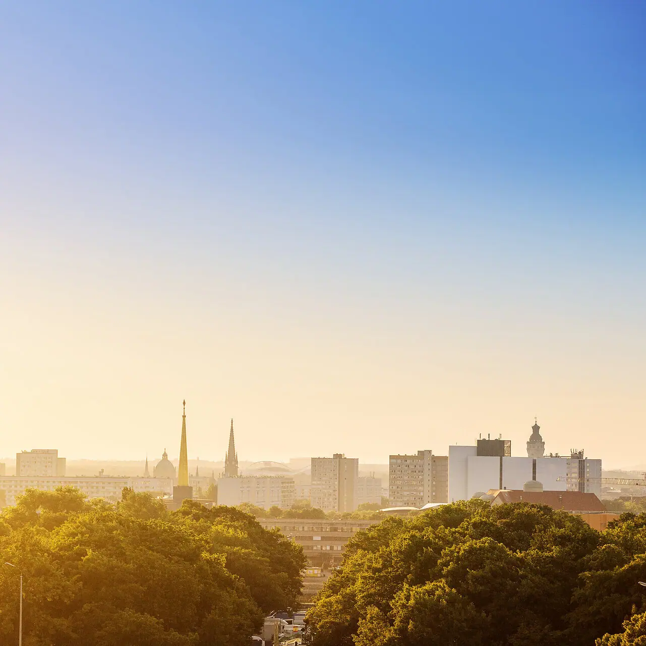 City skyline with trees in the foreground and clear sky in the background.