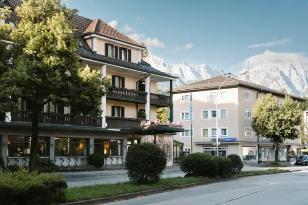 Exterior view of the HENRI Hotel in Garmisch-Partenkirchen, with trees and a road.