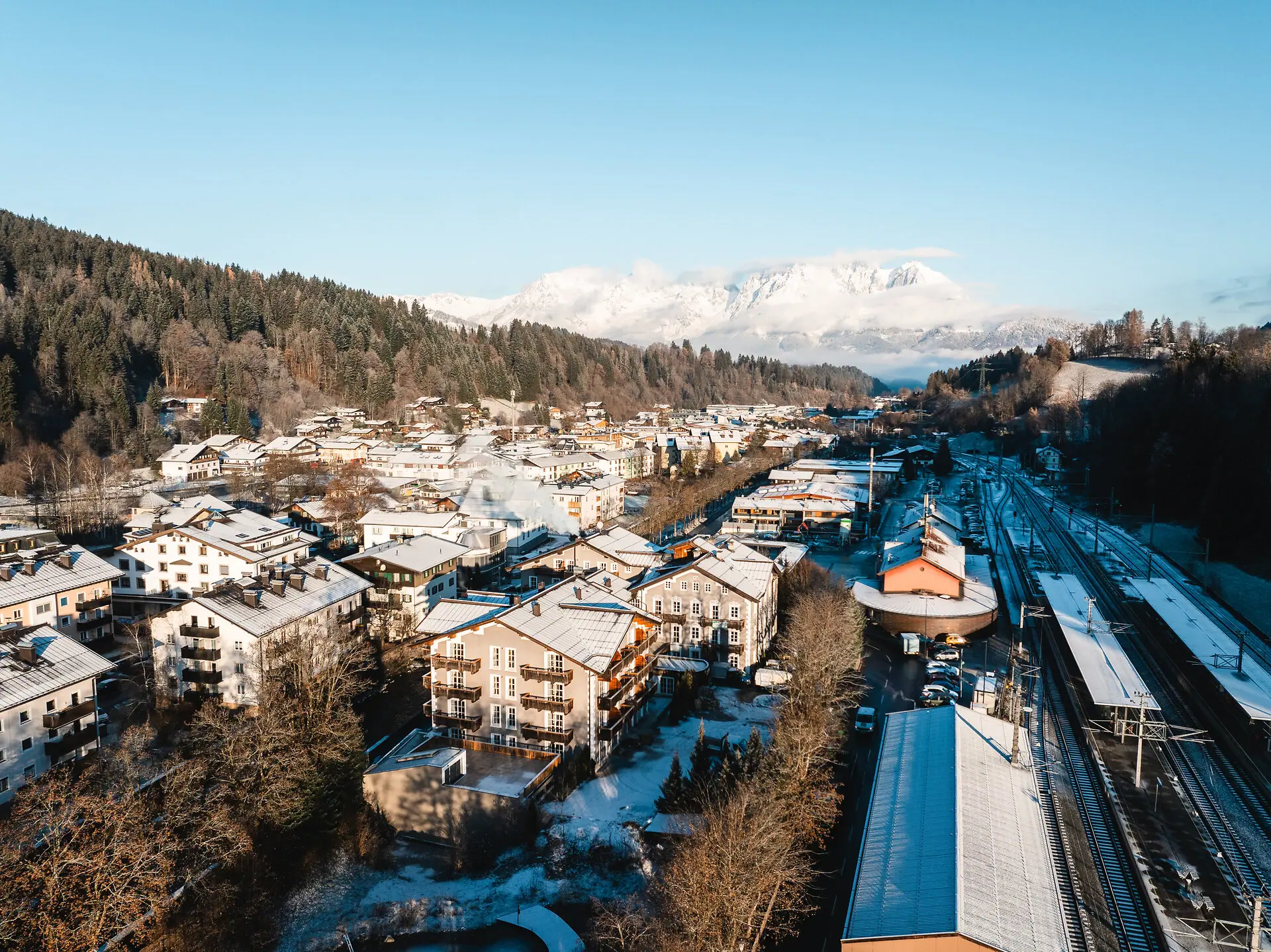 HENRI Kitzbühel: aerial view A snow-covered town in winter, with mountains in the background.