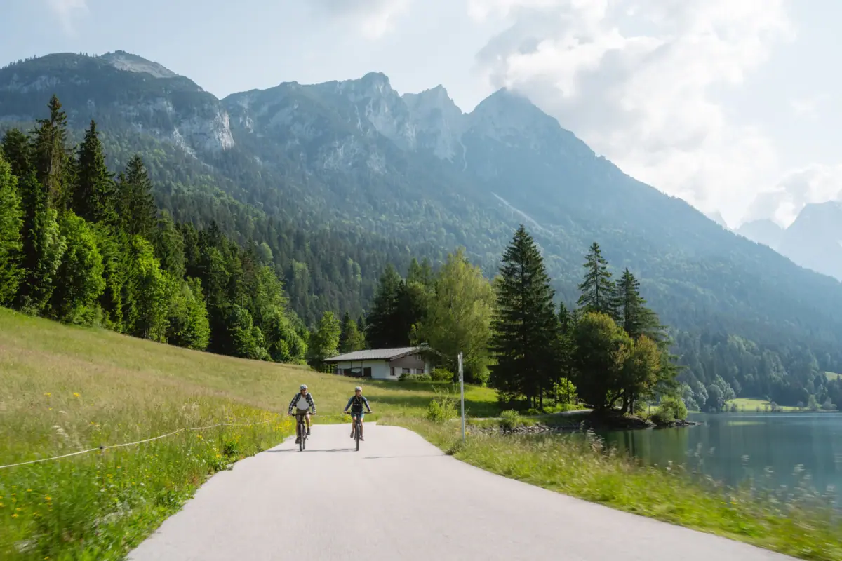 Two people are riding bicycles on a road near a lake.