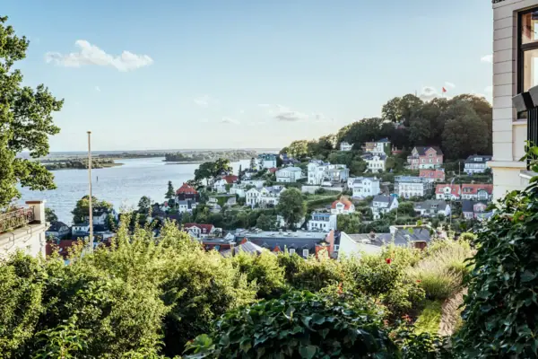 City view with water in the foreground, surrounded by buildings and trees under a cloudy sky.