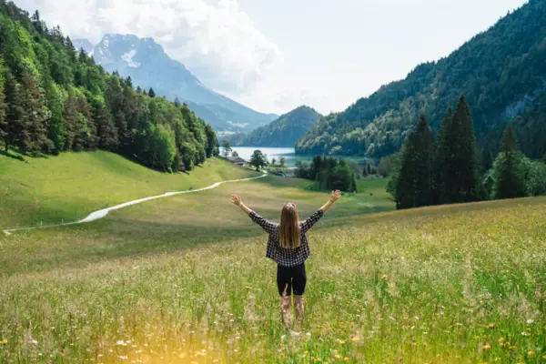 A woman stands in a field with her arms raised.