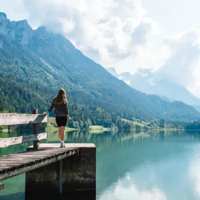 A woman stands on a jetty and looks out over a lake.