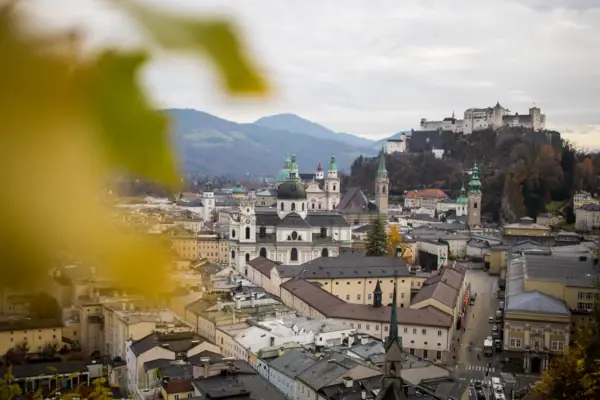 A town with many buildings and a hill with trees and mountains in the background.