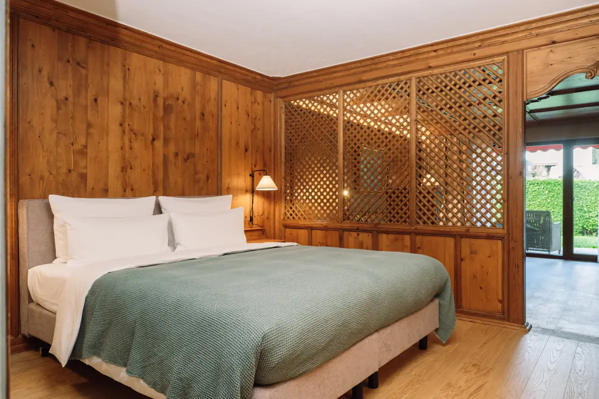A bed with a green duvet against a wood-panelled wall.