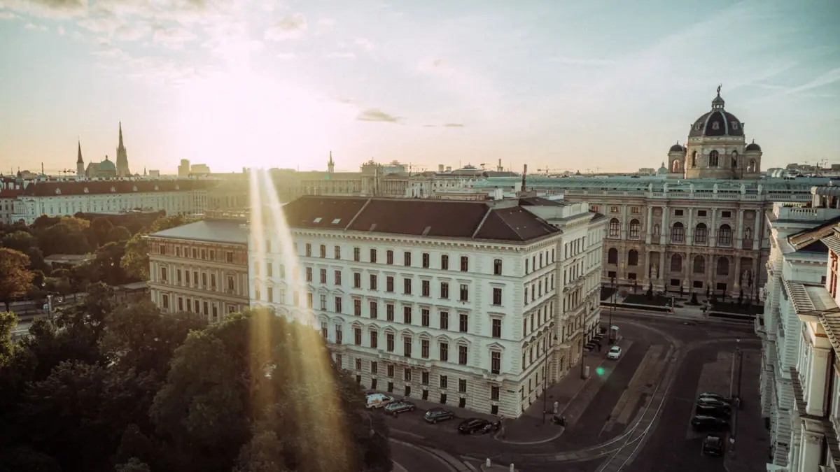 View over Vienna A large white building with lots of windows and a road in the foreground, surrounded by trees.