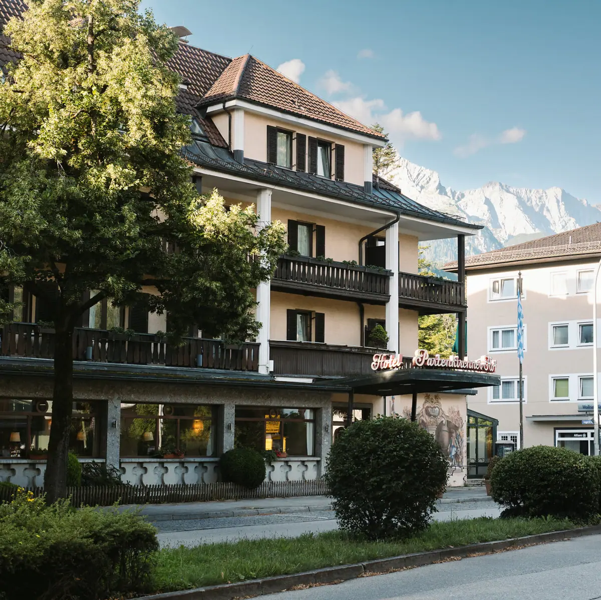 The HENRI Hotel in Garmisch-Partenlkirchen with trees by the roadside and mountains in the background.