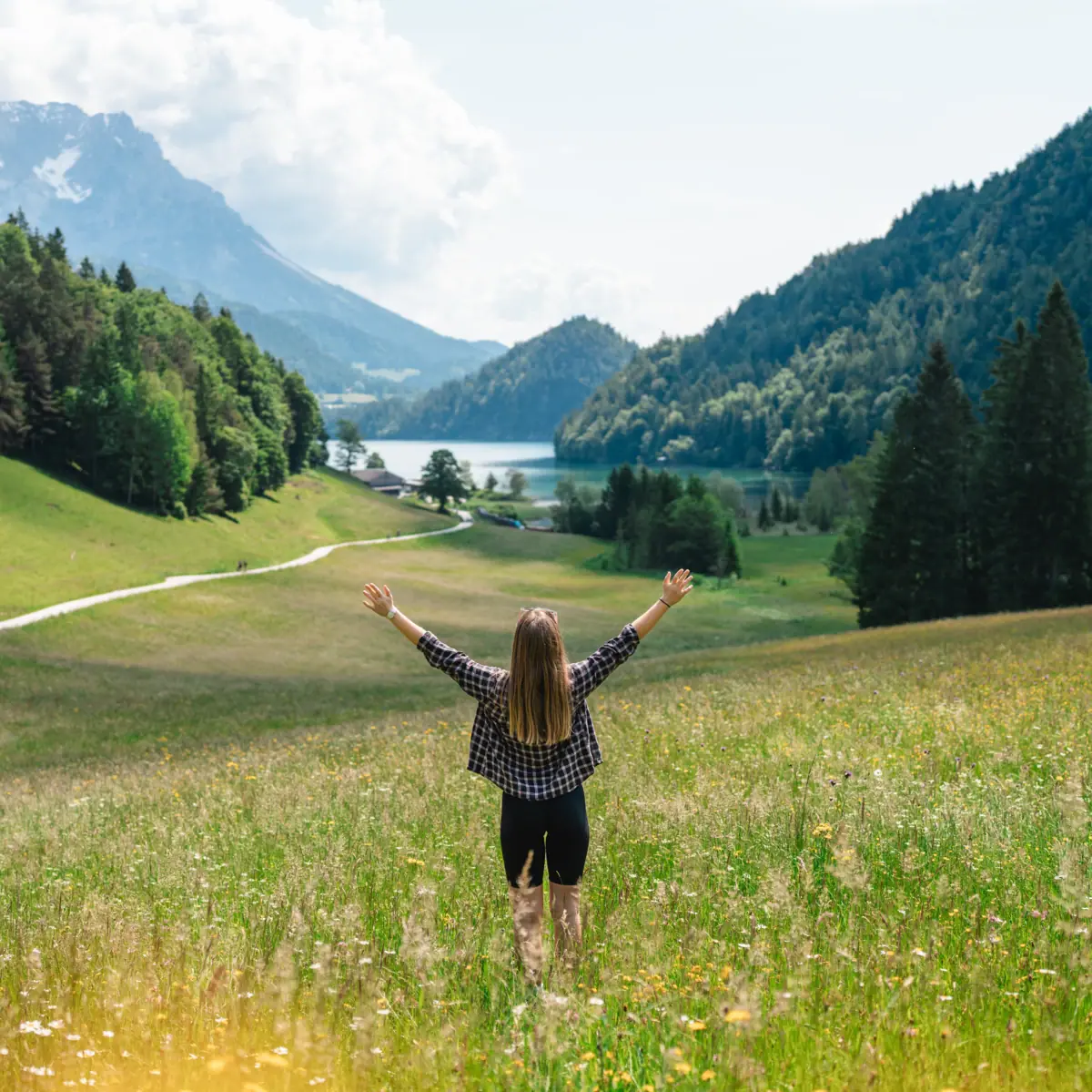 A woman stands in a field and stretches her arms upwards and mountains can be seen in the background.