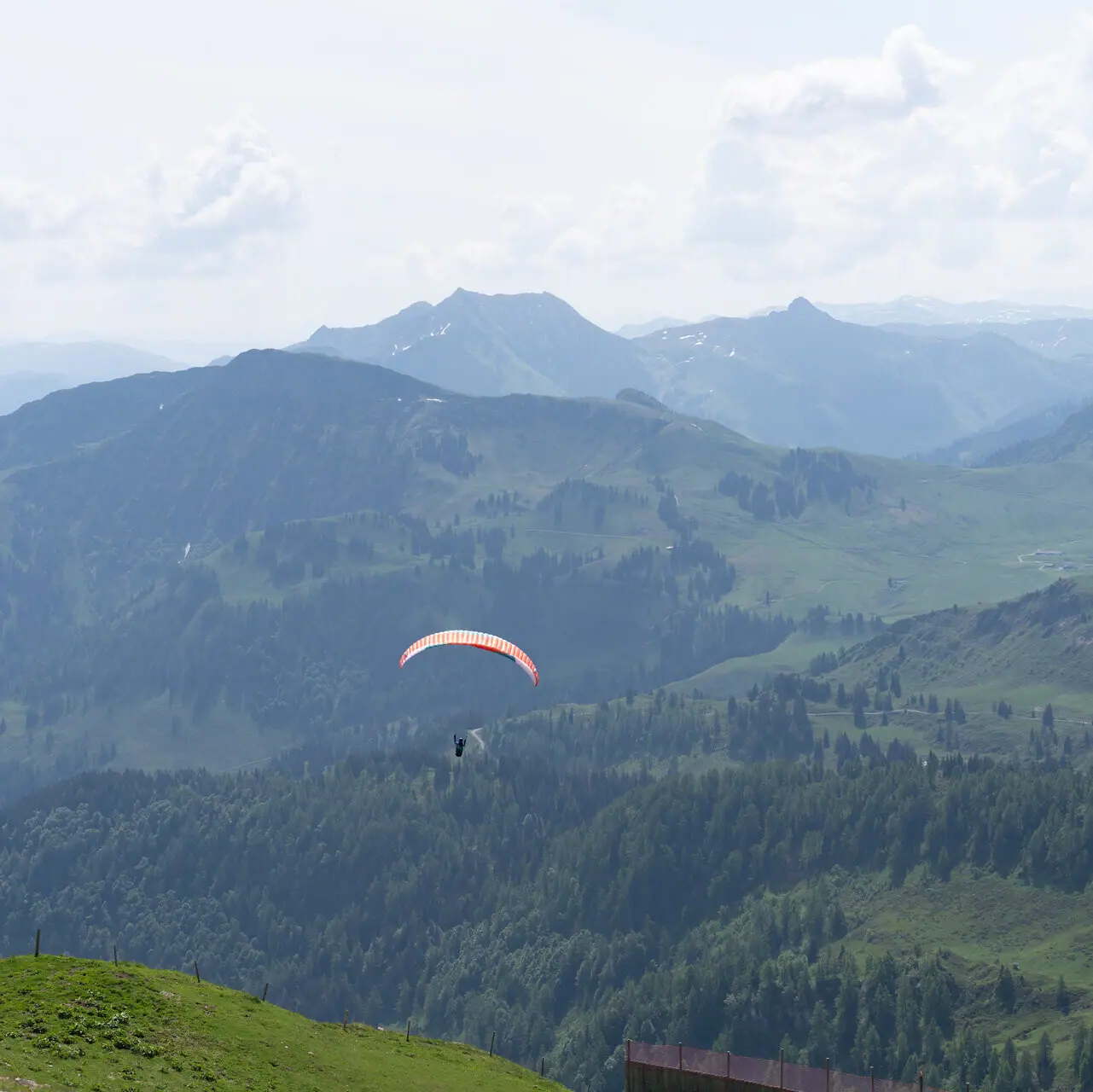 A person paragliding over a valley with mountains and clouds in the background.