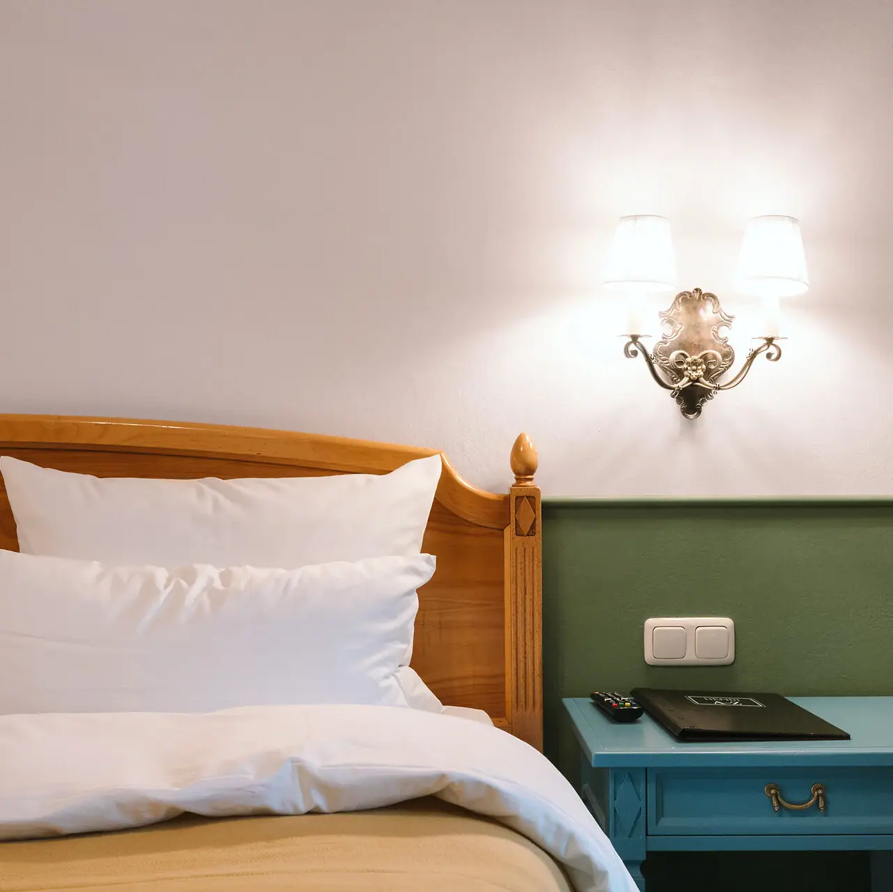 A bed with a wooden headboard in front of a green and white wall in a stylishly furnished hotel room at the HENRI Hotel Garmisch-Partenkirchen.