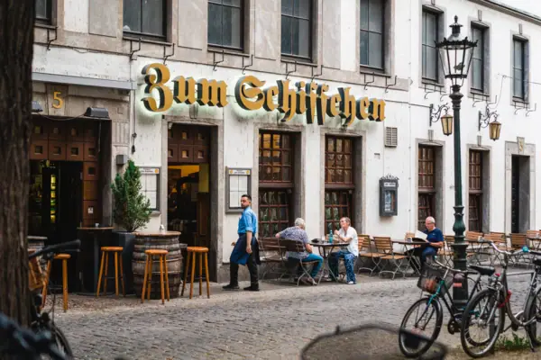 A group of people sit at tables in front of the Zum Schiffchen restaurant.