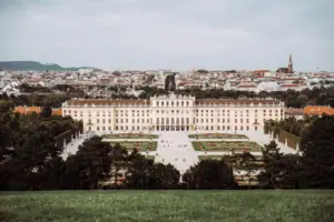 Large building with a courtyard and garden, surrounded by trees and grass under a partly cloudy sky.