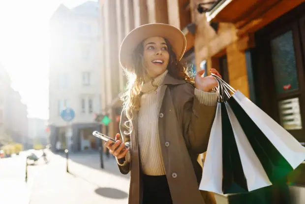 A woman holds shopping bags and smiles.