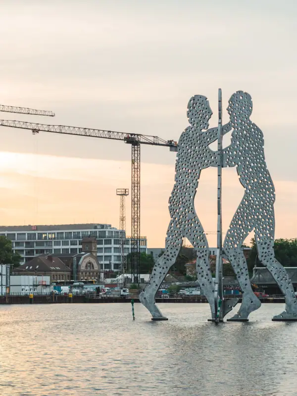 A large metal column with men in the water, with cranes in the background.