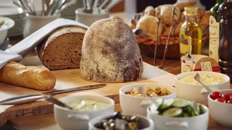 There is a chopping board with bread and a few small bowls of food on a table.