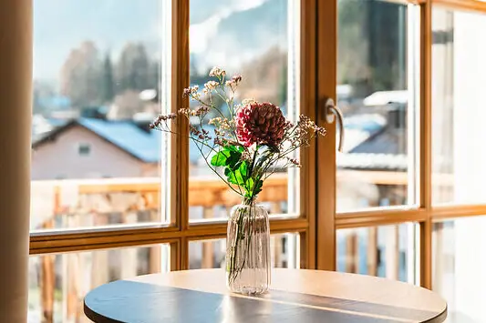 A bouquet of flowers in a vase on a table next to a window.