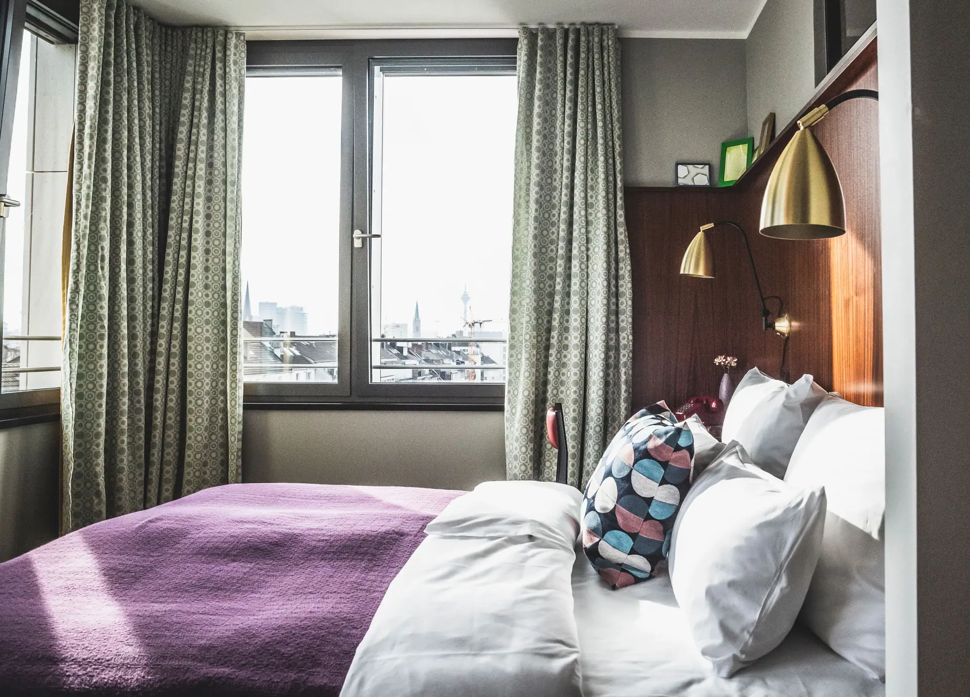 HENRI Düsseldorf A bed with pillows and a lamp in a room with windows.