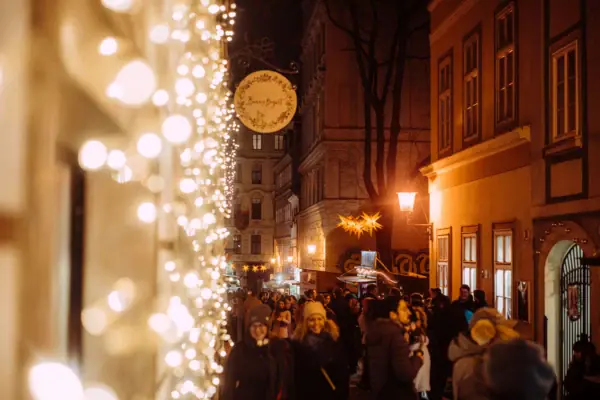 A crowd of people is walking along a street lit up by Christmas lights.