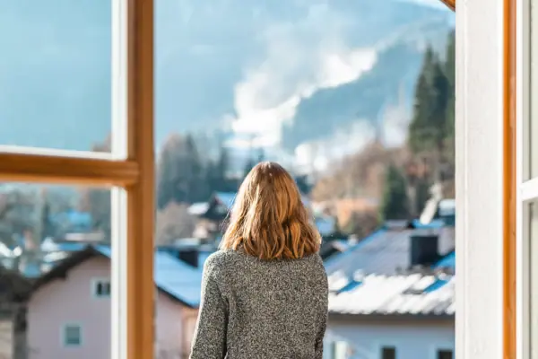 HENRI Kitzbühel Balcony A woman is looking out of a window at a range of mountains.