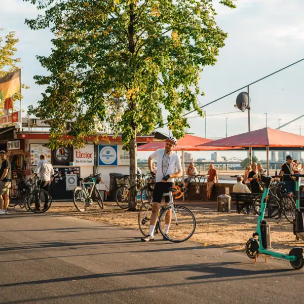 A man on a bicycle on a busy street by the Rhine.