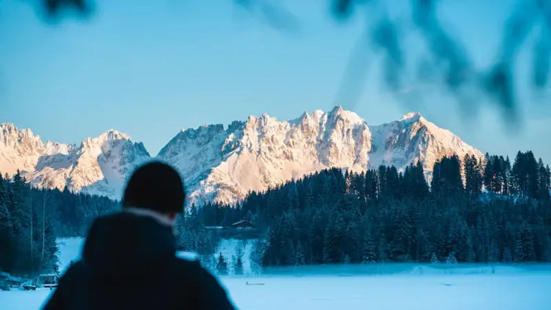 A person stands in front of a snow-covered mountain.