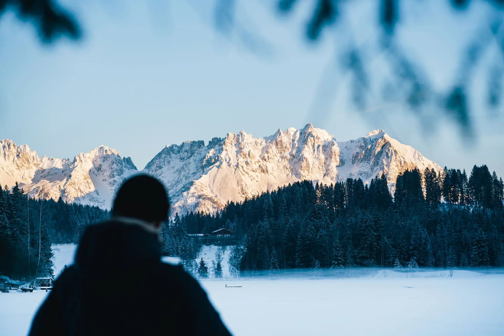 Kitzbühel Alps A person is standing in front of a snow-capped mountain.