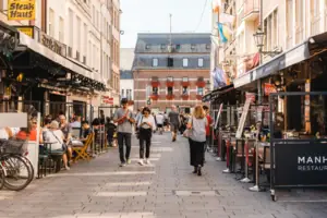 People walking down a sidewalk with others sitting at tables and chairs.