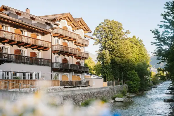 HENRI Kitzbühel A building with balconies and a river in the foreground.