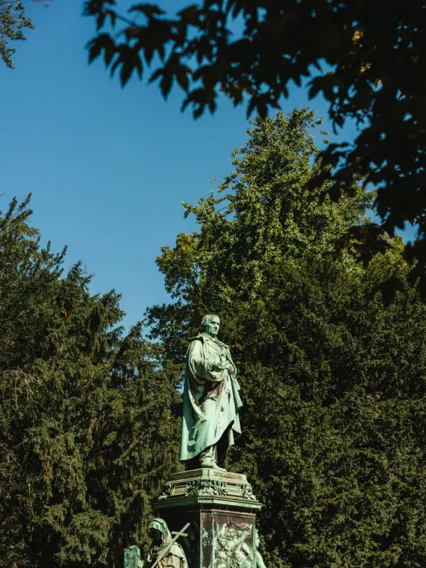 A statue of a man in a robe, standing outdoors against a blue sky.