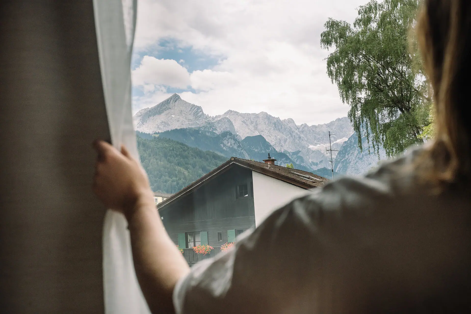 A hand opens a window with a mountain panorama in the background.