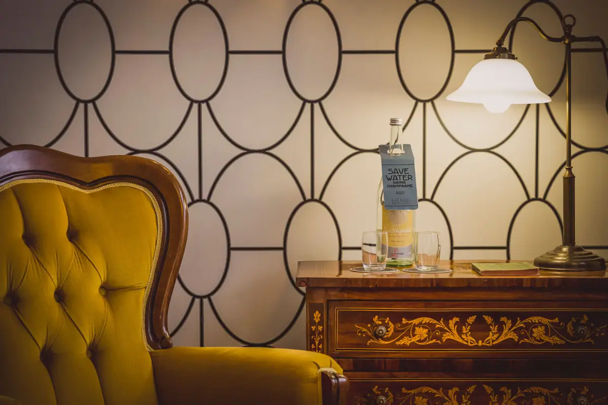 A chair and a table with glasses and a bottle on it.
