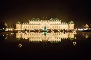 An illuminated building at night, reflected in the water.