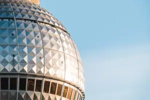 Nahaufnahme der gläsernen Kuppel des Berliner Fernsehturms mit Spiegelungen des Sonnenlichts gegen einen klaren blauen Himmel.