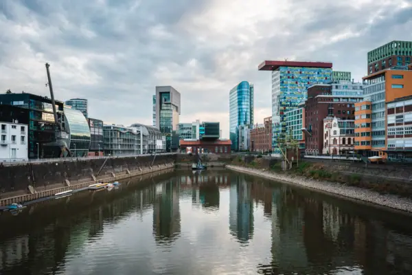 Düsseldorf River with buildings in the background and cloudy sky.