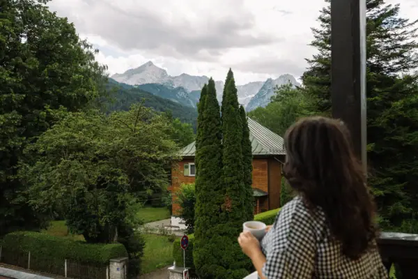 A woman holding a cup of coffee gazes at a mountain range.