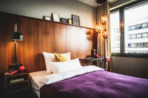 HENRI Düsseldorf Bed with purple duvet and pillows in a room with a window.