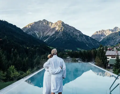 A man and a woman stand on a pool roof with mountains in the background.
