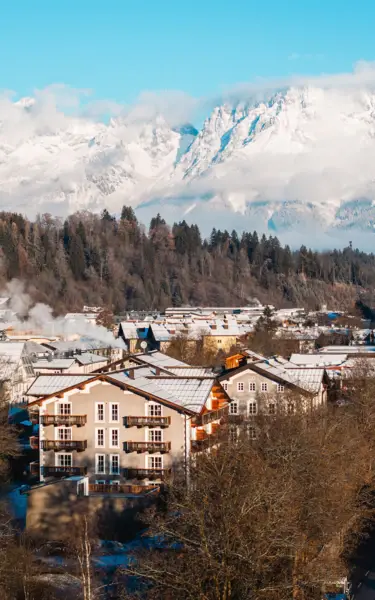 Snow-covered mountains behind a village with houses and trees.