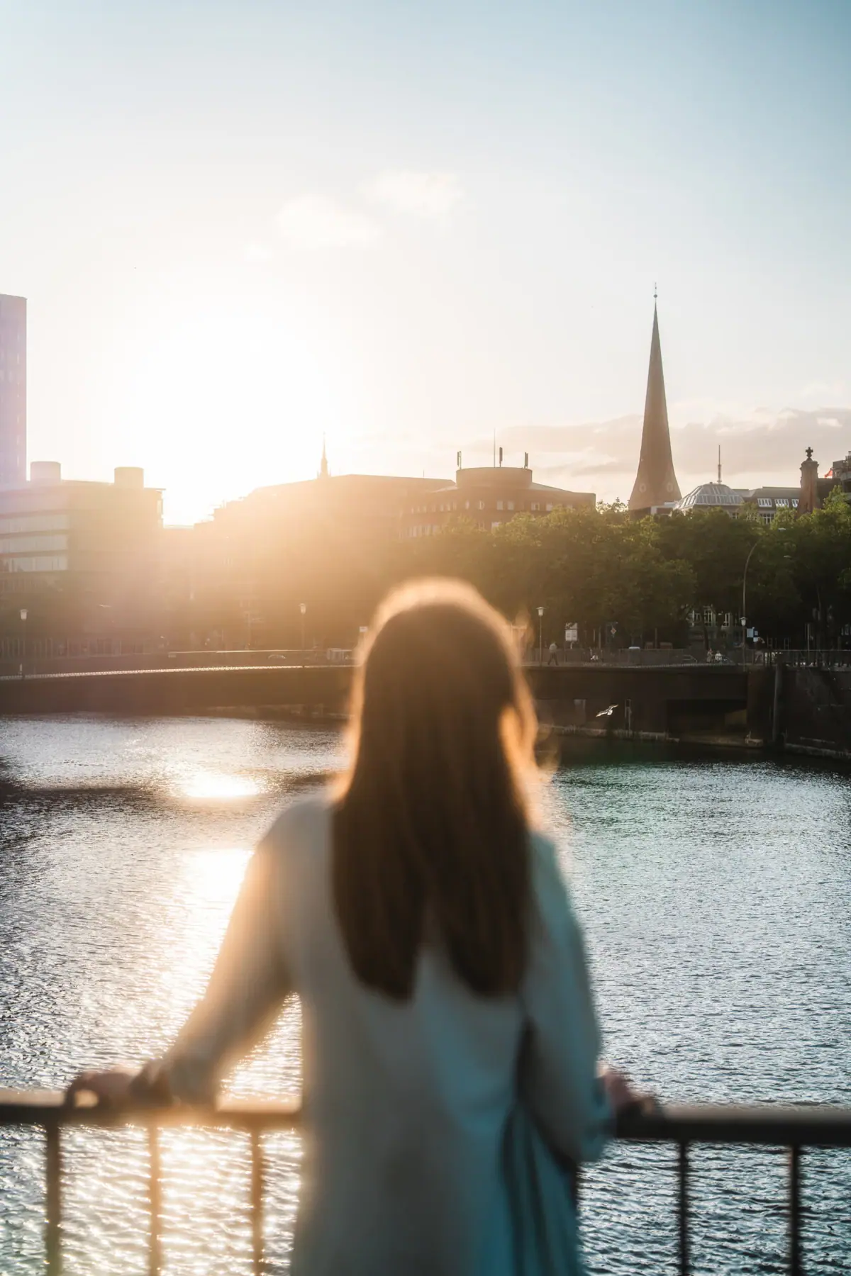 A woman stands on a bridge and looks out over a city.