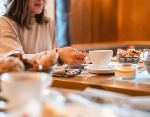 A woman holds a teacup at a breakfast table.