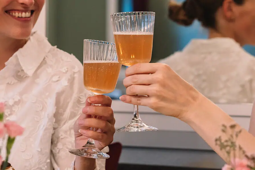 Two women sit at a table and clink glasses of wine.
